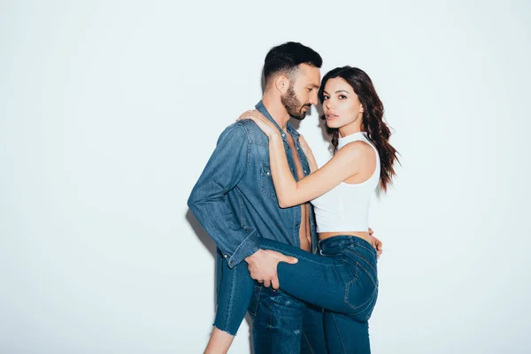 Sensual loving couple in jeans embracing on grey — Stock Photo