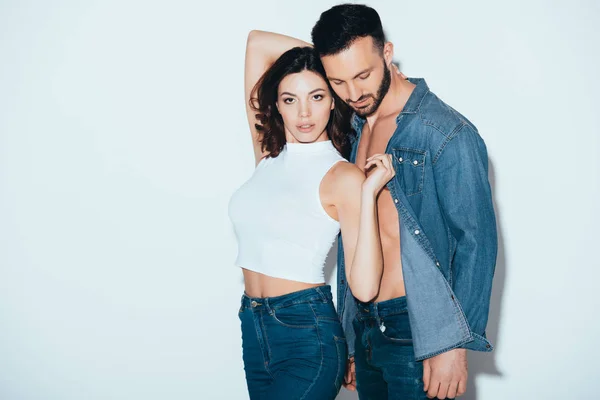 Stylish couple in jeans standing together on grey — Stock Photo