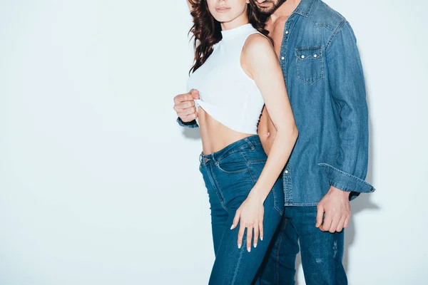 Cropped view of man in jeans undressing girlfriend on grey — Stock Photo