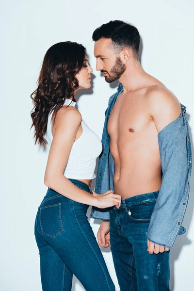 Sensual joven mujer desabrochando jeans en novio en gris - foto de stock