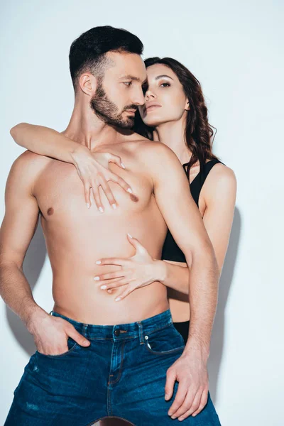 Sensual woman embracing bearded shirtless man on grey — Stock Photo