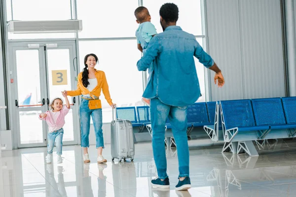 Africano americano feliz mujer con hija caminando hacia marido con hijo en aeropuerto — Stock Photo