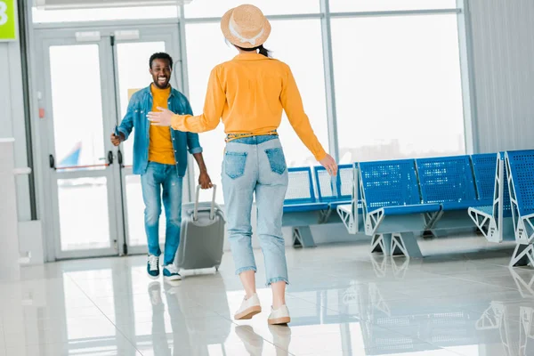 Foyer sélectif de heureux homme afro-américain avec valise marche vers petite amie à l'aéroport — Photo de stock