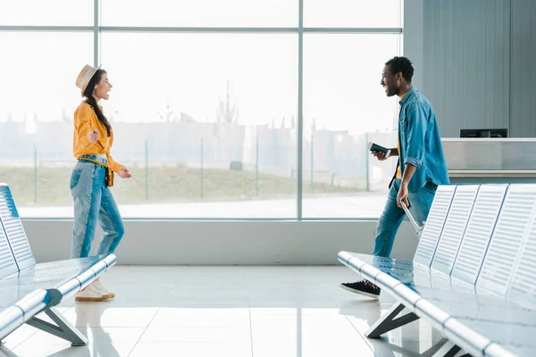 Вид сбоку счастливого африканского мужчины, идущего навстречу улыбающейся подруге в аэропорту — стоковое фото