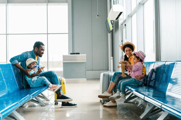 Familia afroamericana feliz sentado en el aeropuerto y esperando el vuelo - foto de stock