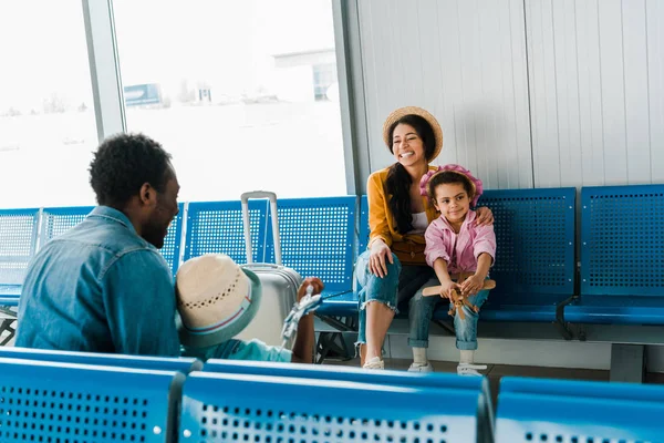 Familia afroamericana sonriente sentada en el aeropuerto y esperando el vuelo - foto de stock