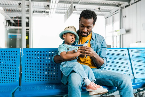 Afrikanisch-amerikanischer Vater und Sohn spielen mit Spielzeugflugzeug in Abflughalle — Stockfoto