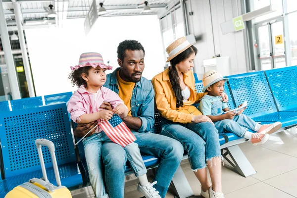 Familia afroamericana sentada en la sala de salida en el aeropuerto con equipaje - foto de stock
