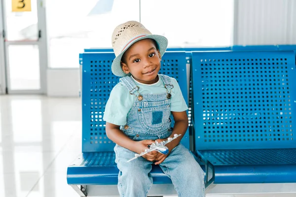 Lindo africano americano chico sentado con juguete avión en aeropuerto - foto de stock
