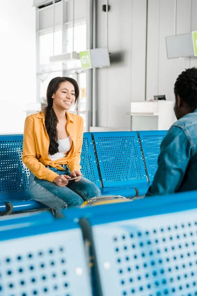 Sonriente afroamericana mujer sentada en la sala de salida con novio - foto de stock