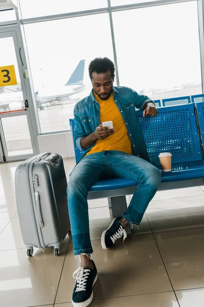 Hombre afroamericano sentado en la sala de salida y el uso de teléfono inteligente - foto de stock