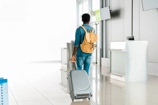 Vista posteriore dell'uomo afroamericano che cammina con bagaglio e zaino in aeroporto — Foto stock
