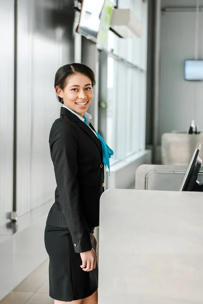 Усміхнений афроамериканський персонал аеропорту в уніформі стоїть на робочому місці — стокове фото