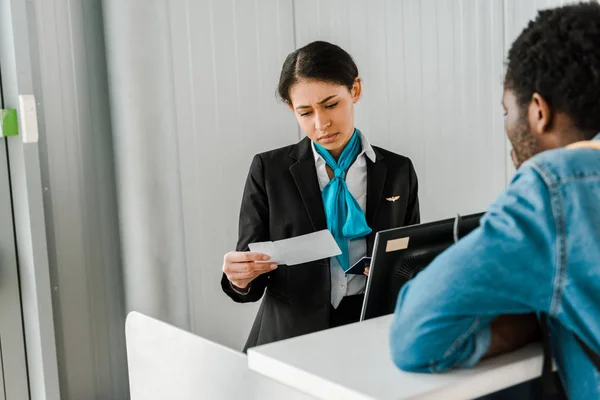 Concentrated african american airport worker looking at air ticket — Stock Photo