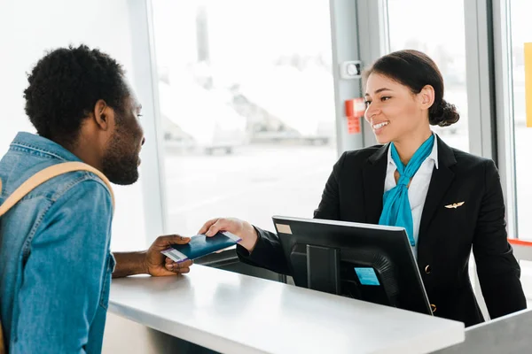 Sorrindo afro-americano trabalhador do aeroporto dando passaporte e bilhete de avião para turista — Fotografia de Stock