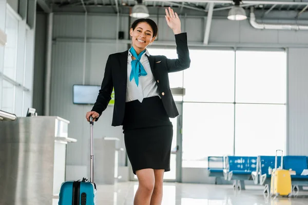 Azafata afroamericana sonriente agitando la mano en el aeropuerto - foto de stock