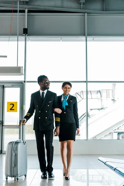 African american pilot and stewardess walking together in airport — Stock Photo