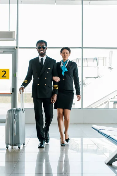 African american pilot and stewardess walking together with baggage in airport — Stock Photo