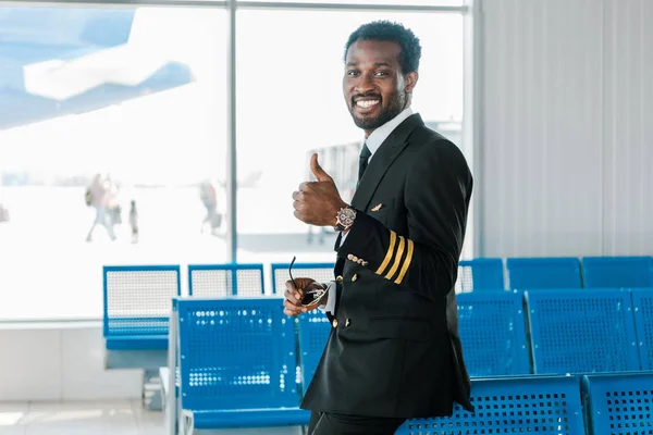 Lächelnder afrikanisch-amerikanischer Pilot zeigt Daumen nach oben in Abflughalle — Stockfoto