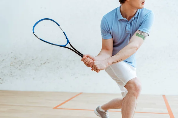 Обрезанный вид спортсмена в синей рубашке поло, играющего в сквош в спорткомплексе — стоковое фото