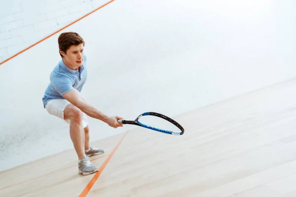 Deportista emocional en polo azul jugando squash en pista de cuatro paredes - foto de stock