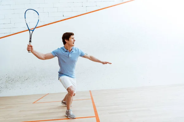 Desportista emocional em camisa de pólo azul jogando squash em quadra de quatro paredes — Fotografia de Stock