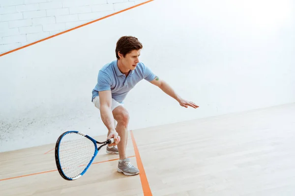Deportista emocional en polo azul jugando squash en pista de cuatro paredes - foto de stock