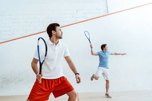 Dois desportistas jogando squash com raquetes em quadra de quatro paredes — Fotografia de Stock