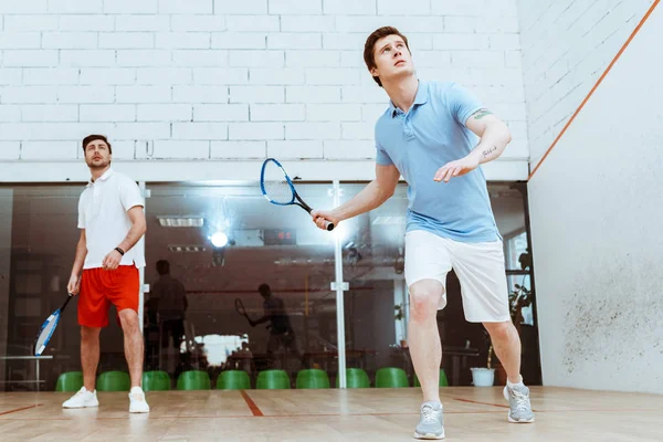 Vue complète de deux sportifs jouant à la squash avec des raquettes dans un court à quatre murs — Photo de stock