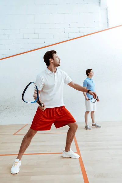 Visão completa de dois desportistas jogando squash com raquetes em quadra de quatro paredes — Fotografia de Stock