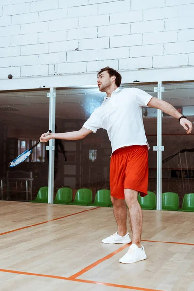 Visão de comprimento total do desportista em shorts vermelhos jogando squash em quadra de quatro paredes — Fotografia de Stock