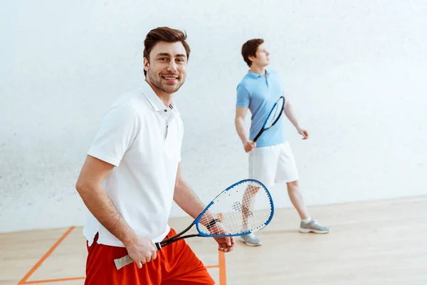 Barbudo jugador de squash con raqueta mirando a la cámara con sonrisa - foto de stock