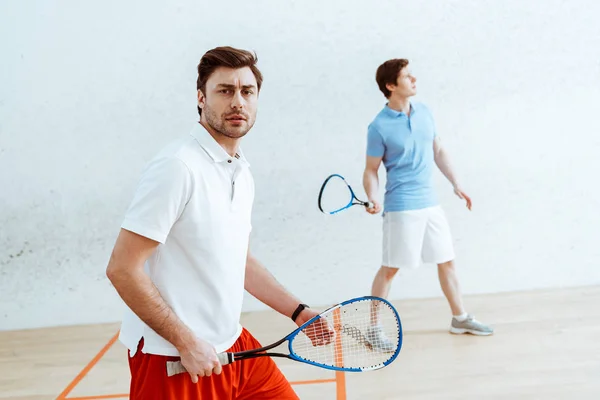 Jogador de squash barbudo com raquete olhando para a câmera — Fotografia de Stock