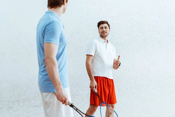Smiling squash player in red shorts showing thumb up to opponent — Stock Photo