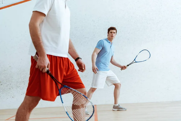 Vista cortada de jogadores de squash com raquetes em quadra de quatro paredes — Fotografia de Stock