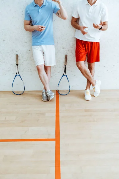 Vista ritagliata di due giocatori di squash in pantaloncini in piedi con gambe incrociate in un campo a quattro pareti — Foto stock