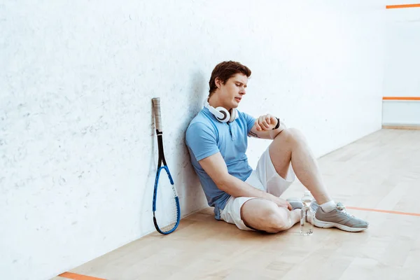 Squash player sitting on floor and looking at smartwatch — Stock Photo