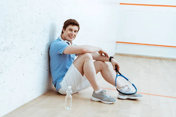 Lachender Squash-Spieler sitzt auf dem Boden und blickt in die Kamera — Stockfoto