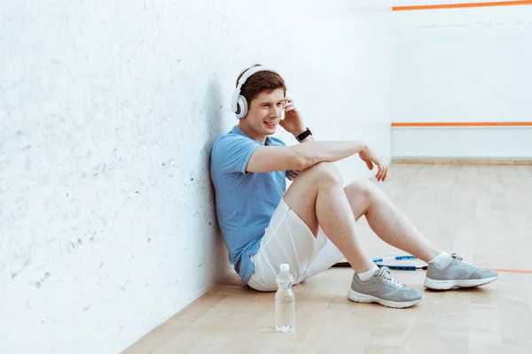 Усміхнений спортсмен сидить на підлозі і слухає музику в навушниках — стокове фото