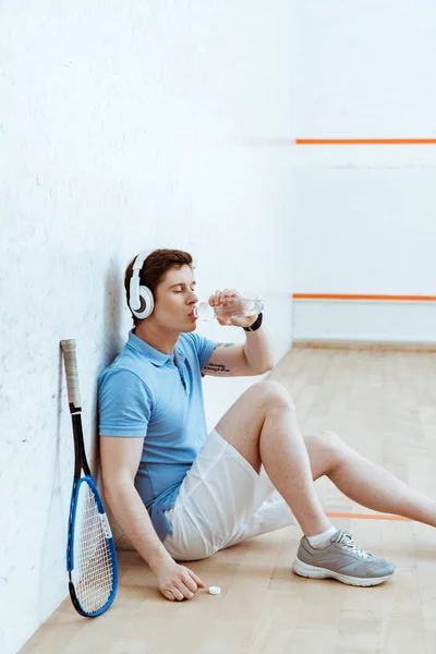 Reproductor de squash escuchando música en auriculares y agua potable - foto de stock