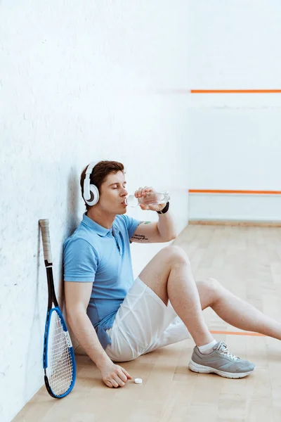 Squash player listening music in headphones and drinking water — Stock Photo