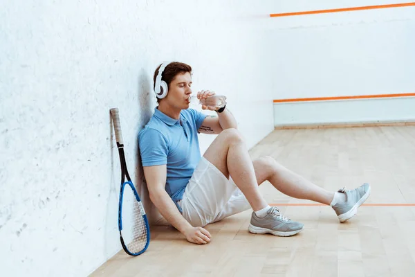 Squash player listening music in headphones and drinking water — Stock Photo