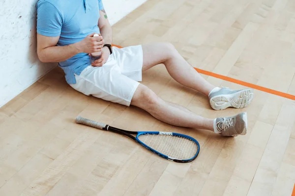 Abgeschnittene Ansicht eines Squash-Spielers, der auf dem Boden sitzt und eine Flasche Wasser in der Hand hält — Stockfoto