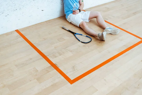 Abgeschnittene Ansicht eines Squash-Spielers, der auf dem Boden sitzt und eine Flasche Wasser in der Hand hält — Stockfoto