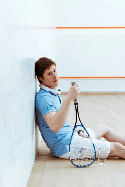Squash jugador de polo azul sentado en el suelo y mirando a la cámara - foto de stock