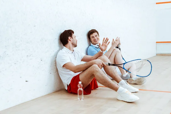 Two squash players talking while sitting on floor in four-walled court — Stock Photo