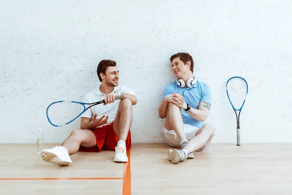 Dois jogadores de squash conversando enquanto sentados no chão em quadra de quatro paredes — Fotografia de Stock