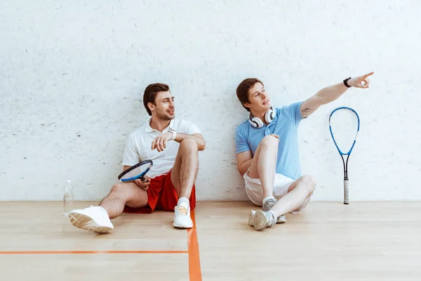 Squash player sitting on floor with friend and pointing with finger — Stock Photo