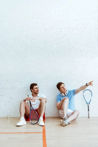 Squash player sitting on floor with friend and pointing with finger — Stock Photo