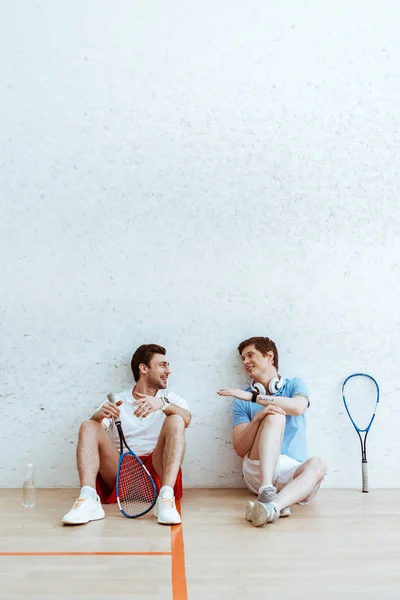 Smiling squash players sitting on floor and talking in four-walled court — Stock Photo